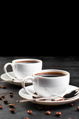 Two cups of coffee on a saucer and coffee beans on a dark background.