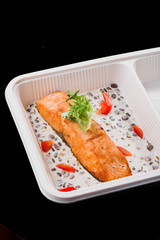 Salmon in a creamy sauce with lentils in an eco box isolated on a black background. Healthy food delivery. Take it on a diet. Fitness food, vegetables, meat and fruits in eco boxes.