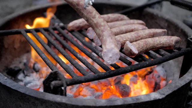Slow motion grilling kielbasa sausage over a campfire of glowing coals.
