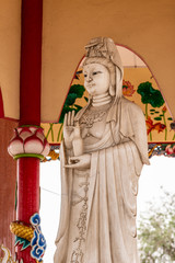 Si Racha, Thailand - March 16, 2019: Closeup of Gray statue of Guan Yin at her open circular shrine on Ko Loi Island. Backed by reds, beiges and whites.