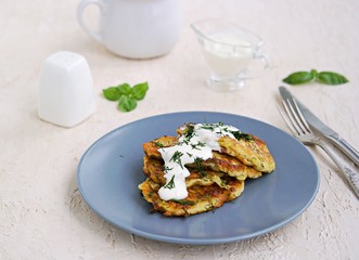 Fritters zucchini with feta cheese on a gray plate on a light concrete background. Served with sour cream. Zucchini recipes. Selective focus.