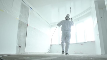 Painter works with airless spray gun when painting ceiling