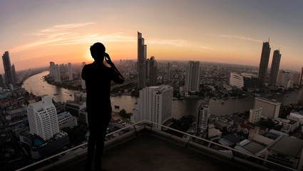 Businessman standing using smart phone on open roof top balcony watching city night view.Business...