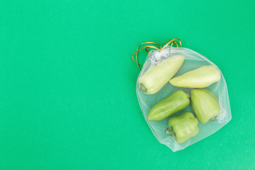 Sweet fresh bell peppers in eco natural bags sewing from mesh cloth on green background with copy...