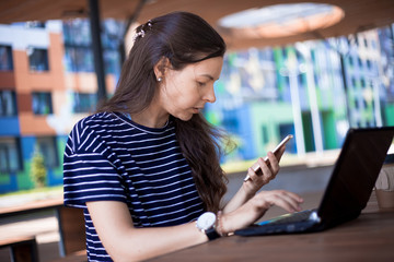 Close-up, portrait of a serious, gently smiling girl student, freelancer, blogger working at a laptop at a wooden table.