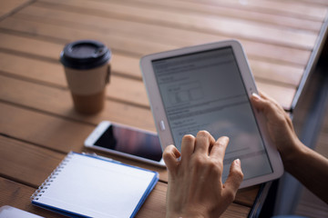 Women's hands with neat manicure and large wristwatch, work with gadgets, tablet, smartphone, papers on a wooden table.