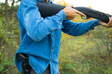 male with semi-automated shotgun and pistol in holster in the autumn forest taking aim