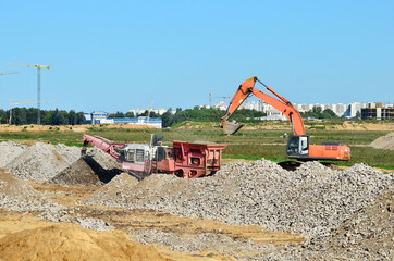 Heavy tracked excavator load stone, old asphalt or concrete waste into a mobile jaw crusher machine. Crushing and processing into gravel for recycling in concrete or cement production.