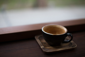 a cup of coffee in a black cup on wood bar 