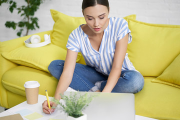 Woman making notes from the laptop at home stock photo