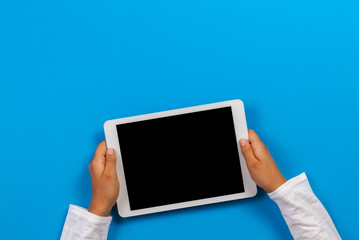 Kid hand holding white tablet computer on light blue background