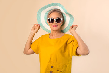 adult elderly woman in a hat on a beige background in sunglasses