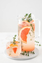 Lemonade with grapefruit and thyme in a glass jug on light background.