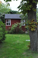 Fototapeta na wymiar Schwedenrote Gartenlaube mit zwei Fenstern und Baumstamm