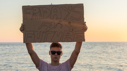 Pupil holding a cardboard poster with the text-Fridays for future, on the sea background.