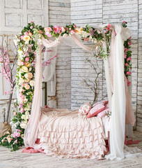 Decorated bedroom in natural style with a lot of flowers. Bed, braided and twined with flowers.