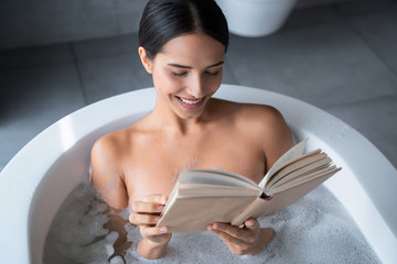 Happy lady reading a book in the bathroom