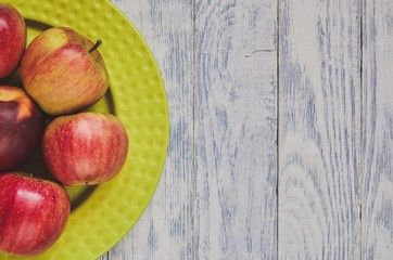 Fresh red fruits. Apples on a green plate on a wooden background.
