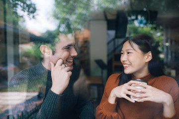 Couple having coffee on a date talking and smile together. shot through window glass