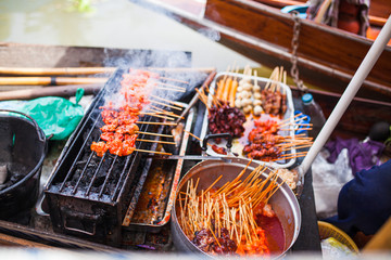 asian streedfood bbq grill in an wooden canoe on amphawa floating market in thailand on a river...