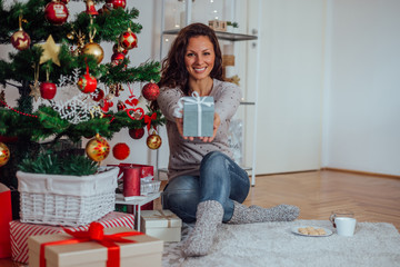 Portrait of a cute woman giving Christmas gift to the camera, at cozy home.