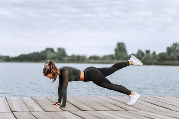 Fit woman doing leg lift plank pose outdoors.