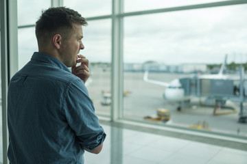 Caucasian young man is afraid to flight standing in terminal near window