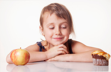 Unhealthy eating or healthy eating. Cute little girl choosing between apples and sweets