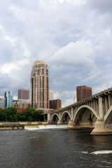 Urban cityscape and modern architecture background. Cloudy sky over Minneapolis downtown skyline and Third Avenue Bridge above Mississippi river, vertical composition. Midwest USA, Minnesota.