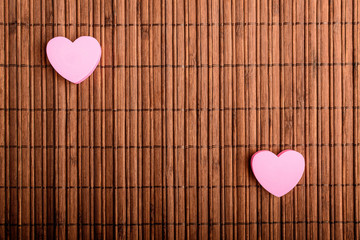 Two pink hearts on a brown bamboo table decoration, top view or flat lay with selective focus