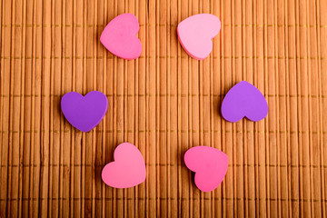 Six pink and mauve hearts on a brown bamboo table decoration displayed in a round circle, top view with space for text on the right side, selective focus