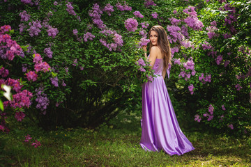 Obraz na płótnie Canvas Authentic young woman standing near the blooming tree of lilac . Looking at camera