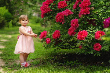 Little sad girl standing near the blooming bush. Spring garden. copy space