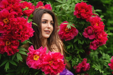 Pretty woman among big red flowers in park or garden