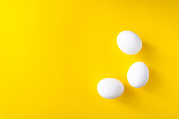 Three white eggs on a yellow background. World egg day concept............