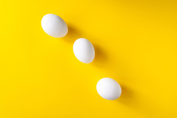 Three white eggs on a yellow background. International world egg day concept..
