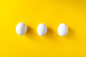 Three white eggs on a yellow background. International world egg day concept