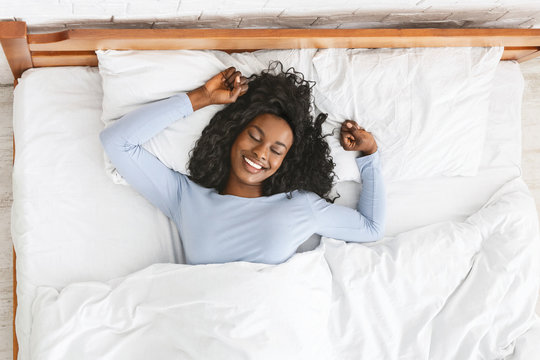 Top view of smiling woman stretching in bed