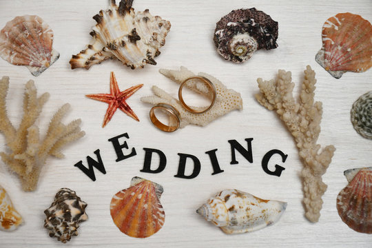 A writing „Wedding“, two wedding rings lying on a coral branch, two other coral branches, a starfish & ten cockleshells