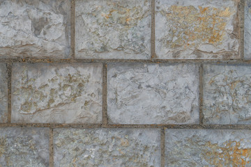Wall of gray pale blocks with cement joints and cracks close up. Abstract original background.