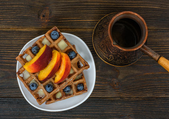 Chocolate Belgian waffles with fruits and coffee pot on wooden background. Delicious breakfast. Top view