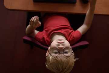 Funny blond boy in glasses resting at a laptop. Internet and preschooler. Top view