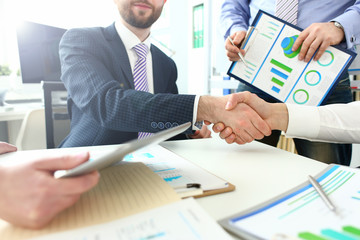 Close-up of witty workers approving agreement between two representatives of different corporations. Bearded boss shaking hands with young manager. Company meeting concept