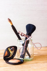MAKEUP SET WITH EYELASH CURLER, BRUSHES AND EYE SHADOW ON WOODEN TABLE