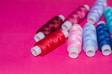 needlework, craft, sewing and tailoring concept - row of colorful thread spools on pink background, flat lay, top view