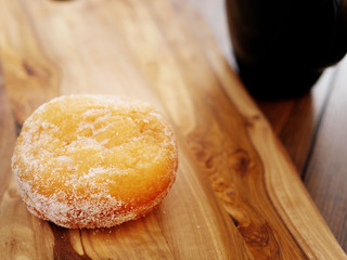 One doughnut with sugar glaze on a wooden background. Warm tones. Black tea cup, Concept breakfast.