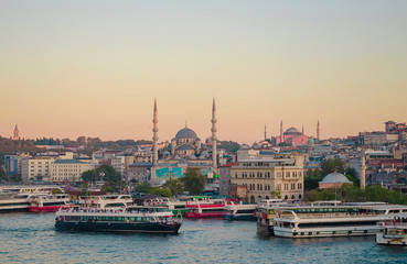 Fototapeta premium Sunset sky. Tourist pleasure boats on pier in Golden Horn Bay. View of famous Hagia (Aya) Sofia Museum and the New Mosque. Popular tourist destination. Turkey, Istanbul, Bosphorus