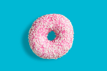 One pink donut with white sprinkle on bllue background. Fresh donut poured with pink glaze.