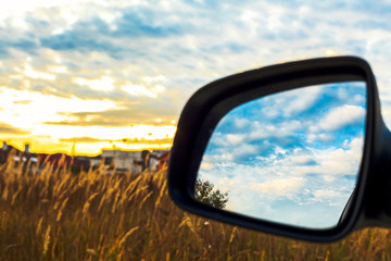 Autumn landscape. Beautiful sunset in sideview car mirror. Reflection of the sky in a car mirror