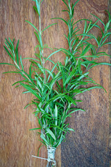 Bound sprigs of rosemary lie on a wooden table. View from above. Vertical.